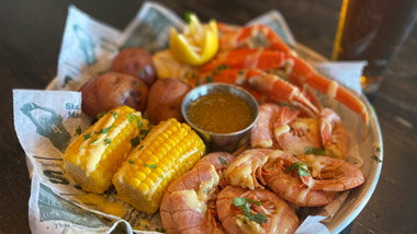 basket of crab, shrimp, corn and potatoes with a beer