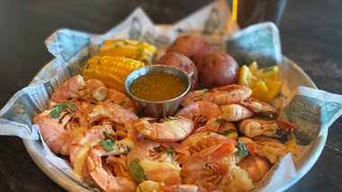 a basket of shrimp, corn and potatoes with a beer