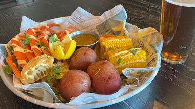 crab legs, corn and potatoes with a beer