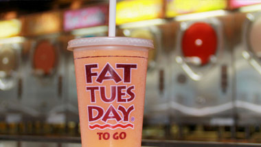 Fat Tuesday To Go cup with blurred daiquiri machines in the background