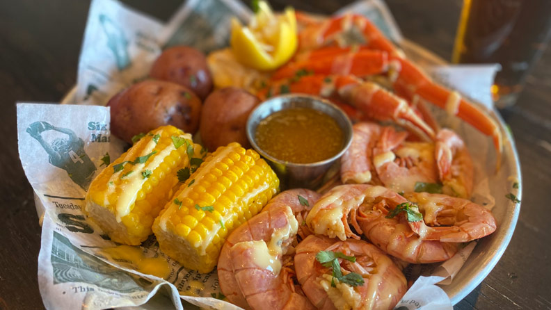 crab, shrimp, corn and potatoes in a basket with a beer